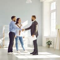 Un agente immobiliare stringe la mano a una giovane coppia in una stanza luminosa e moderna.