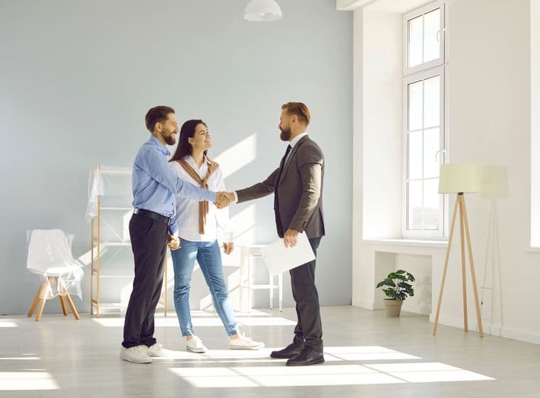 Un agente immobiliare stringe la mano a una giovane coppia in una stanza luminosa e moderna.