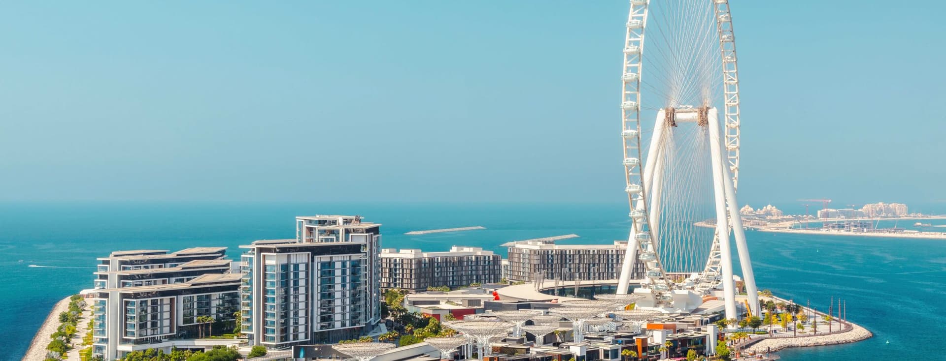 Luftaufnahme von Bluewaters Island, Dubai, mit dem Ain Dubai Riesenrad, Gebäuden und einer Brücke über türkisfarbenes Wasser.