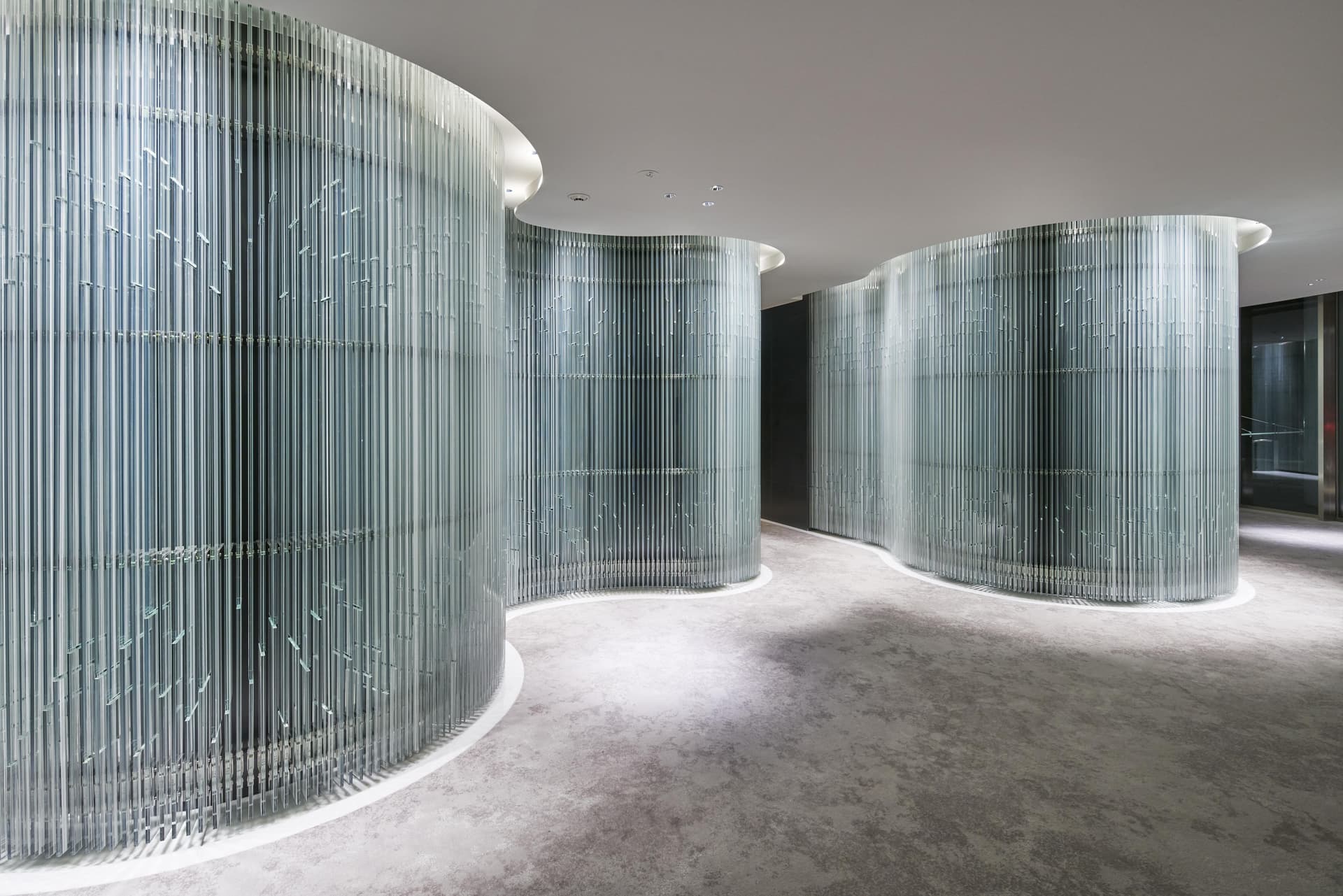 Intérieur moderne avec des murs incurvés en verre et une moquette grise. Les murs sont constitués de tiges de verre verticales.