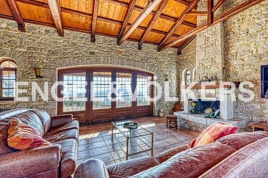 Living room with stone walls, wood ceiling, and brown leather sofas. Large windows overlook the ocean. A stone fireplace is on the right.