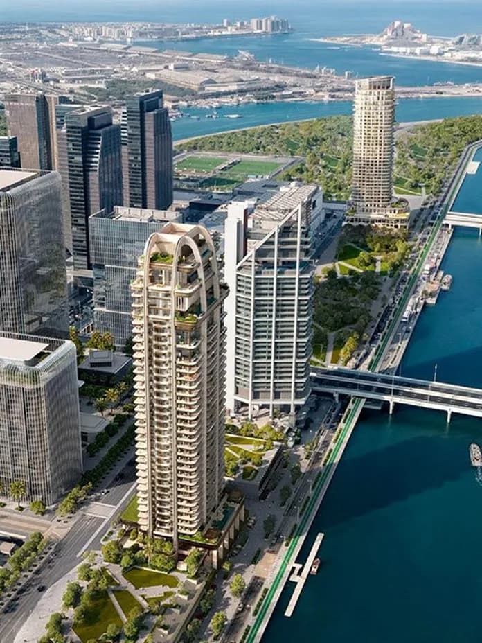 Aerial view of a modern city along a turquoise canal, with tall glass skyscrapers, bridges, and green waterfront parks.