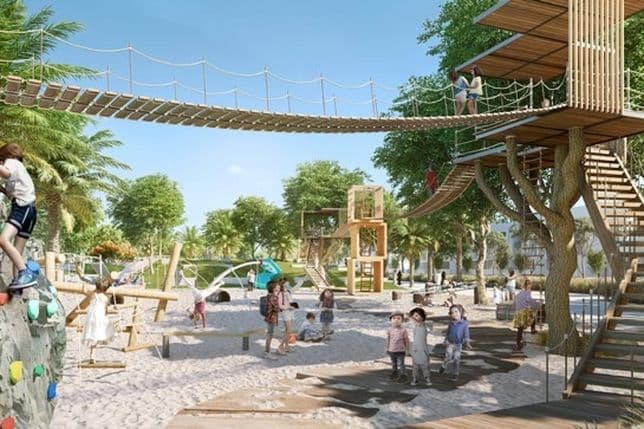 Children playing in an outdoor adventure park with ropes, climbing walls, and wooden structures amidst trees under a clear blue sky.