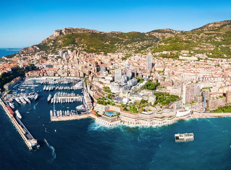 Aerial view of Monaco, a city-state on the French Riviera, with a harbor full of yachts and buildings stretching up a green hillside.