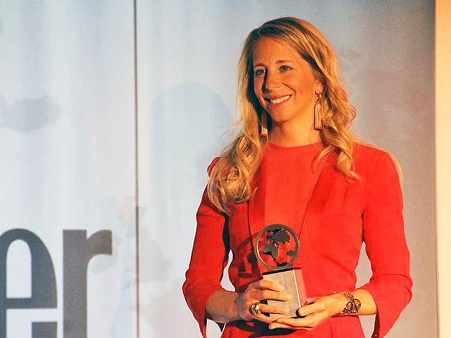 Ninon Völkers in a red dress holds the Human Values Condé Nast Traveler Award on stage.