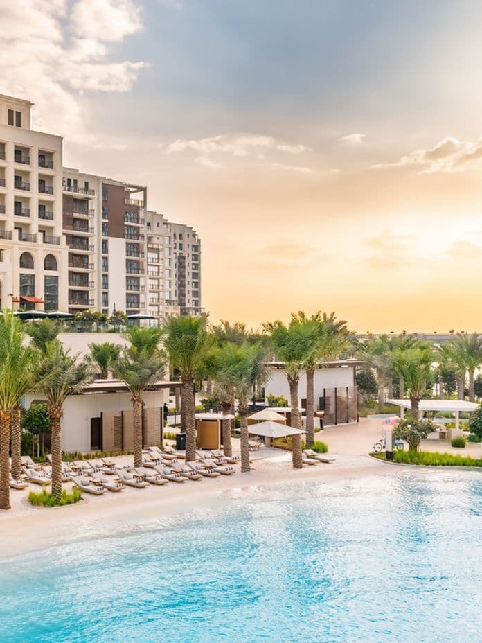 Luxuriöses Strandresort mit Palmen, Liegestühlen und einem großen Pool vor dem Hintergrund eines Sonnenuntergangshimmels.