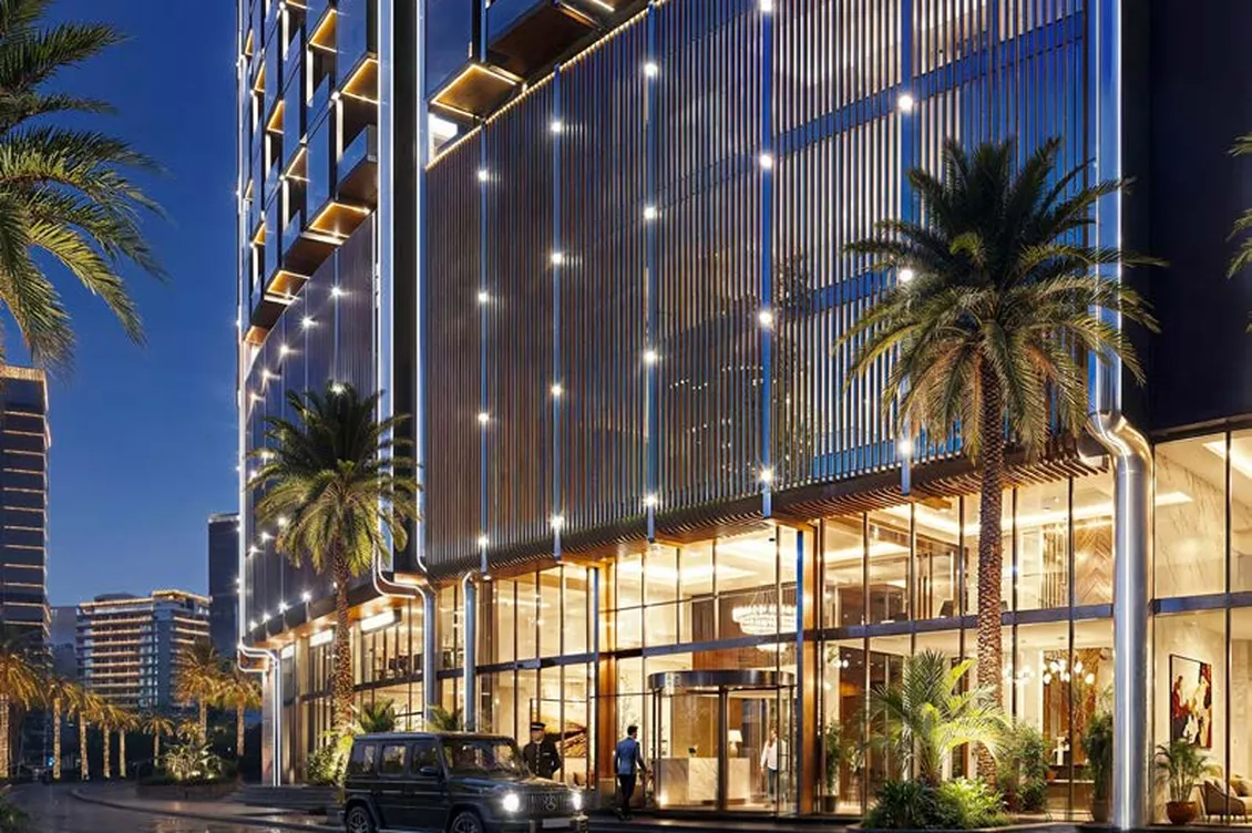 Night scene of a glass-fronted modern building with vertical light strips, palm trees, and a black SUV parked near the illuminated entrance. AI-generated image