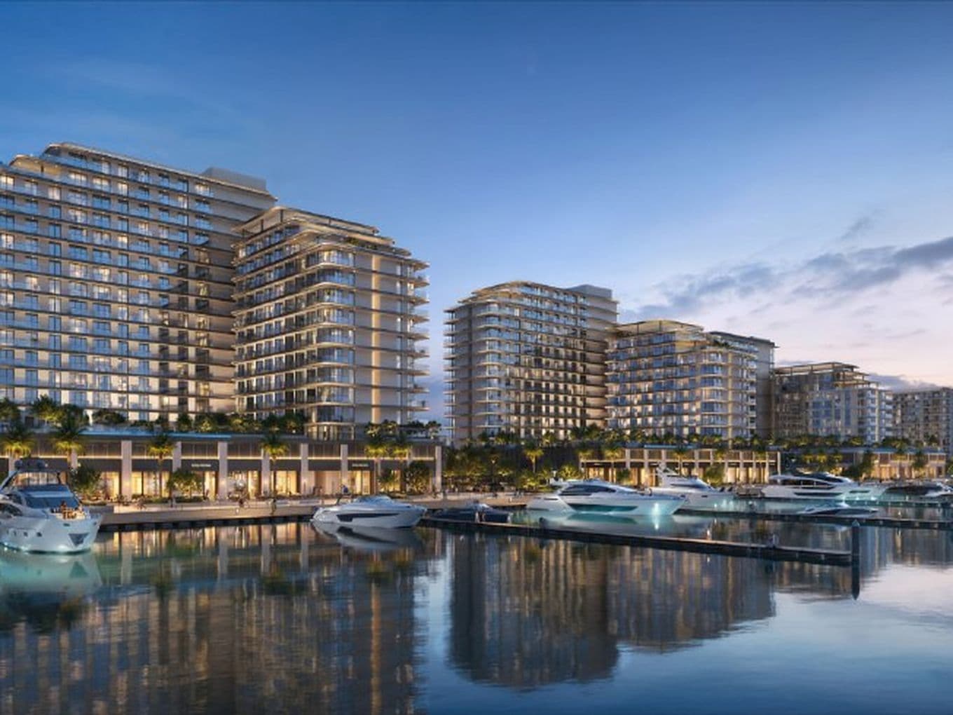 Modern waterfront buildings with illuminated windows at dusk, yachts docked along the calm water reflecting the evening sky.