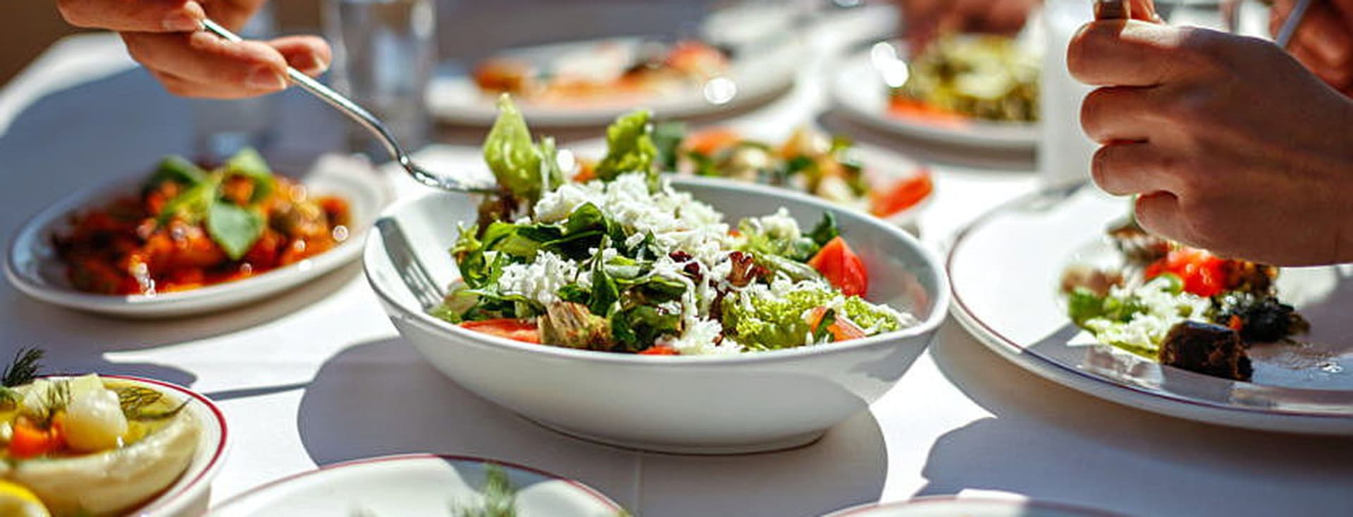 Se ven nueve platos de cocina mediterránea, ensaladas, y dos personas comiendo