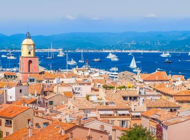 Saint-Tropez cityscape with terracotta rooftops, a clock tower, and boats on the blue sea.