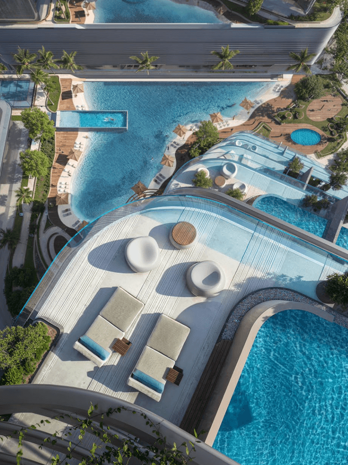 Aerial view of a modern rooftop pool area with lounge chairs and circular seating, overlooking a larger pool and landscaped surroundings.