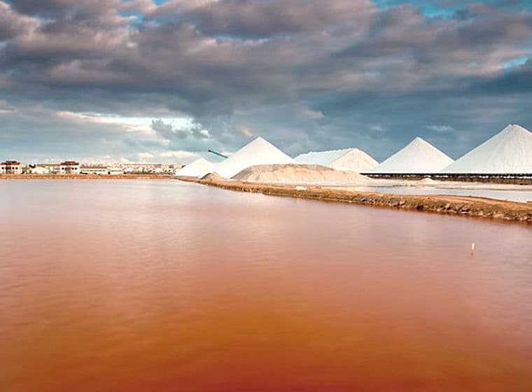 Vista panoràmica de la llacuna rosa amb cinc dunes de sal i un cel ennuvolat.