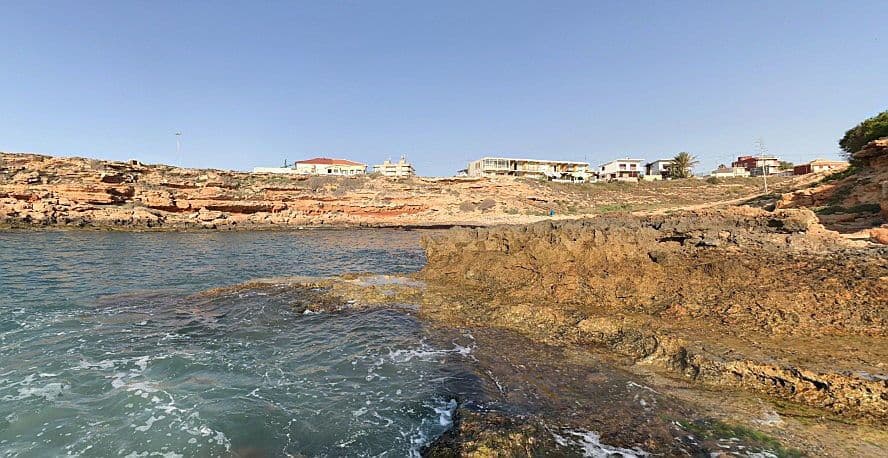 Vista de la Cala de la Guineu amb roques i edificis.