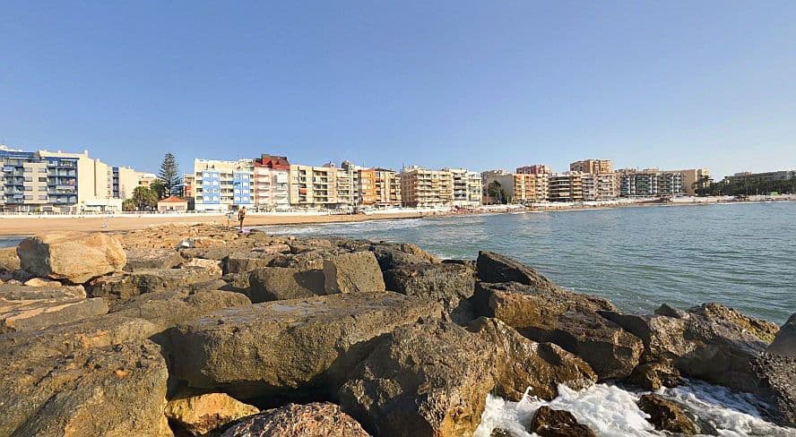 Platja dels Bojos Torrevella 2, vistes des de les roques, del mar i edificis a l'horitzó.