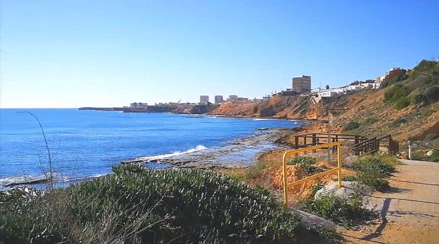 Vista de Cala del Moro Torrevella, camí costaner a la dreta i edificis a l'horitzó.
