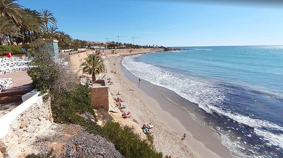 Vistes de la platja de La Mata a Torrevieja amb roques, palmeres i gent prenent el sol.