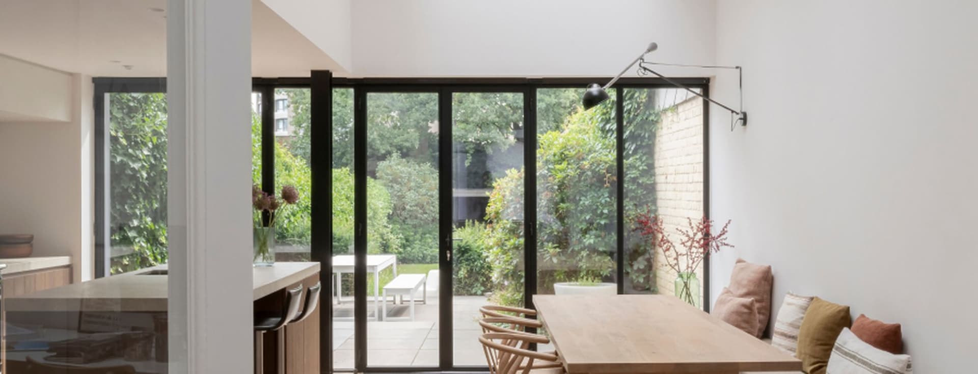 Heller Essbereich mit Holzbänken, Esstisch aus Eichenholz, Oberlichtern, bodentiefen Gartenfenstern, Fischgrätenparkett und eingebauten Sitzbänken mit Kissen, die eine nahtlose Verbindung zwischen Innen und Außen schaffen