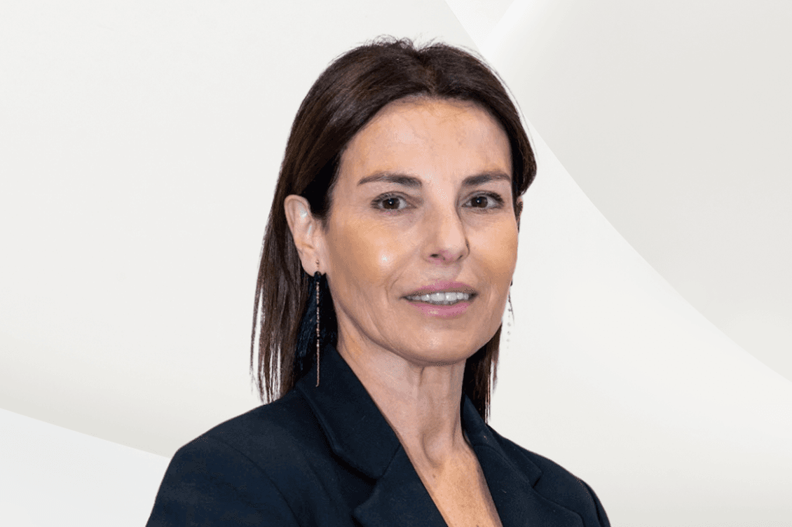 Headshot of a smiling woman with brown hair, wearing a black blazer and white top, against a white background.