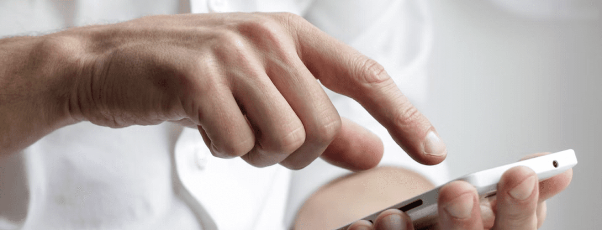 Uma pessoa de camisa branca usa um smartphone branco com o dedo.