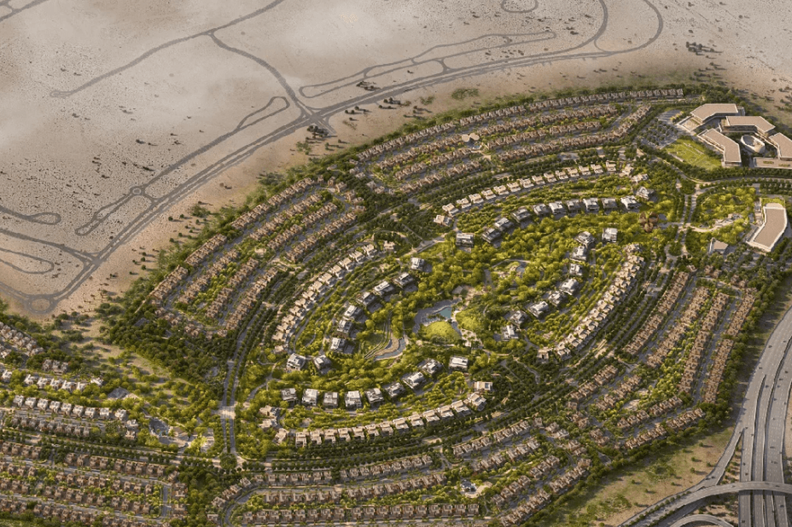 Aerial view of a circular, green residential development surrounded by desert, with roads and pathways connecting the community.