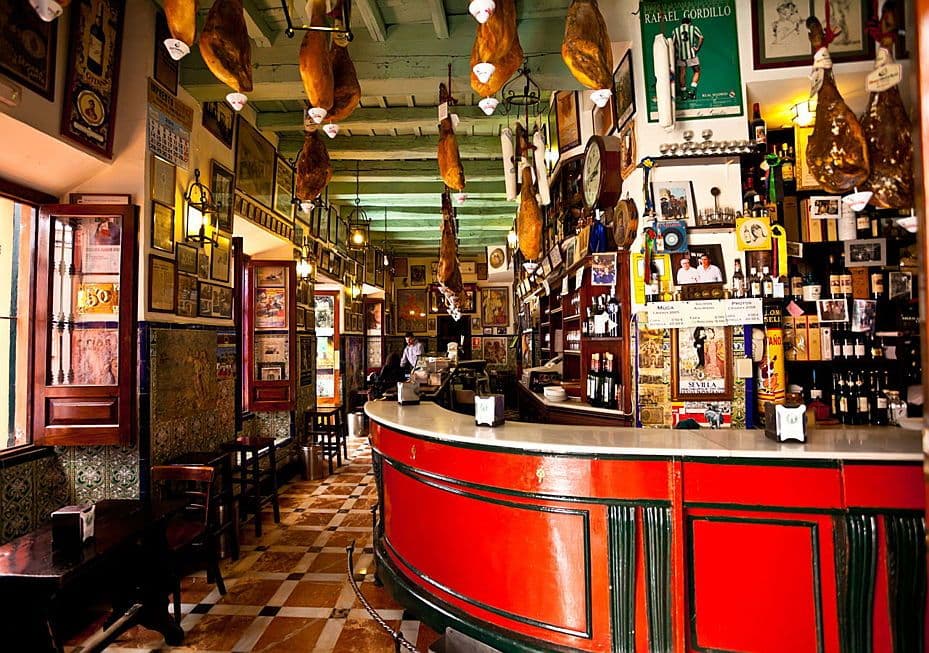 Pub. Imagen del interior de un pub vacío con una barra roja y jamón colgado del techo.