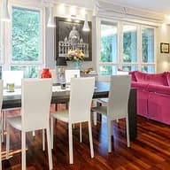 Bright living room with wood floors, a dining table with white chairs, and a pink sofa near a bookcase and TV.