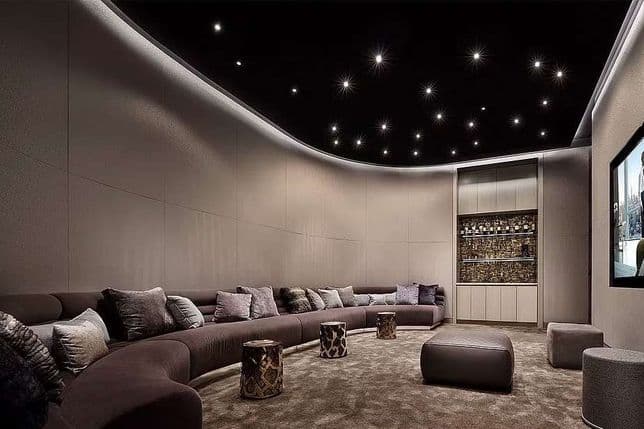 Luxurious home theater with a curved sectional sofa, plush pillows, a backlit bar, and a starry ceiling, featuring a large wall-mounted screen.