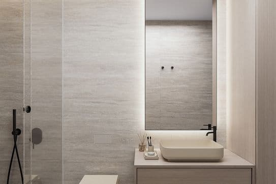 Minimalist beige bathroom with a glass-walled shower, wall-hung toilet, and a wood vanity topped by a rectangular sink beneath a backlit mirror.