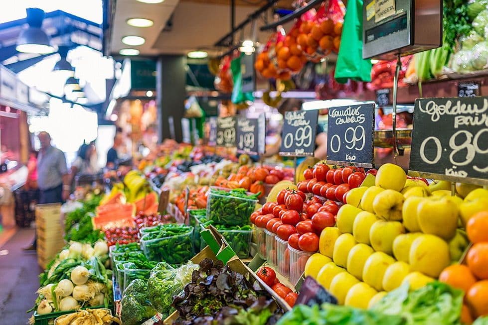 Puestos de frutas y verduras frescas en un supermercado, exhibidos con sus precios.