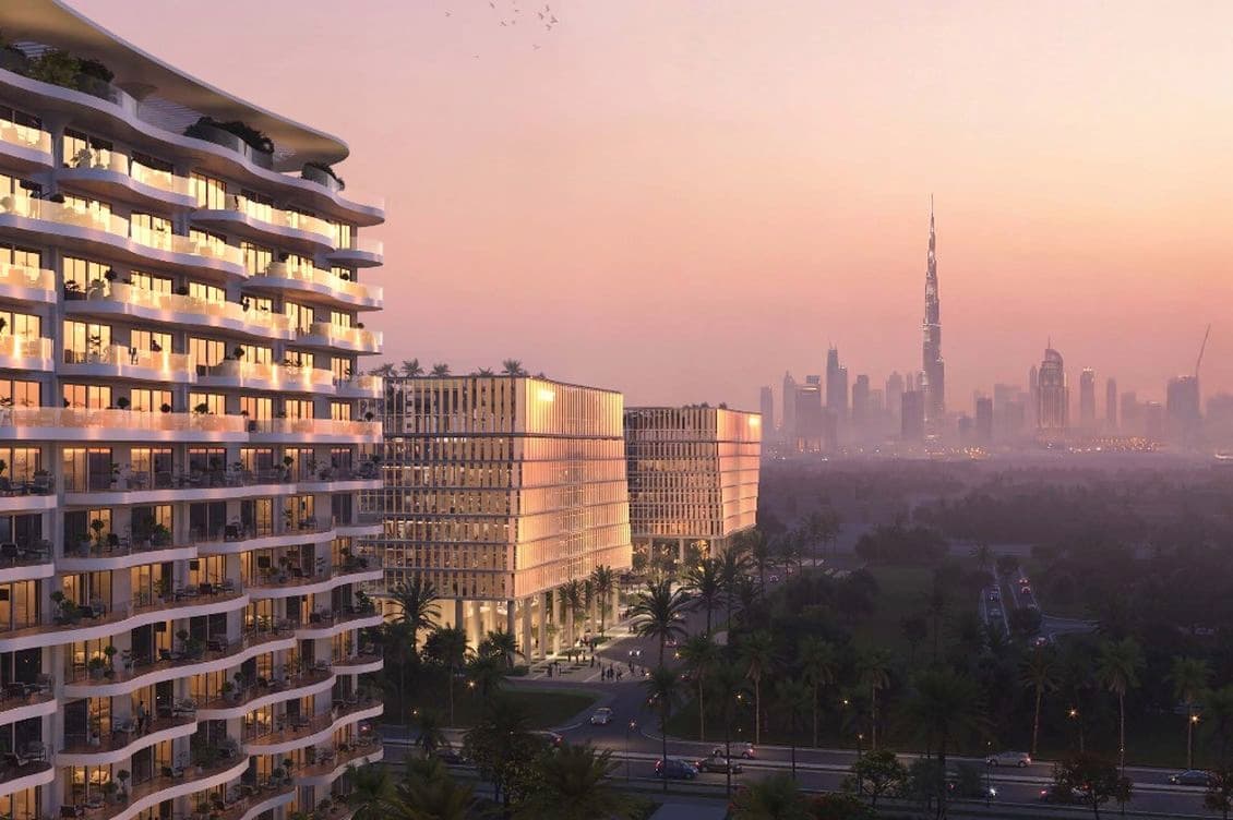 Sunset view of a curved glass-fronted residential tower with balconies, palm-lined streets, and a distant skyline topped by a tall spire.