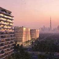 Sunset view of a curved glass-fronted residential tower with balconies, palm-lined streets, and a distant skyline topped by a tall spire.