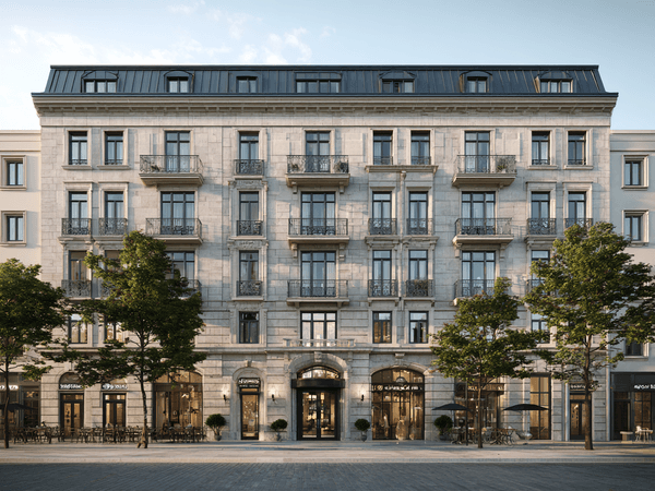 Elegant multi-story stone building with wrought iron balconies, large windows, and ground-floor shops, flanked by leafy trees under a clear sky.