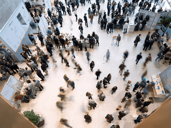 Aerial view of a busy conference or trade show with many attendees walking and interacting at booths, creating motion blur.