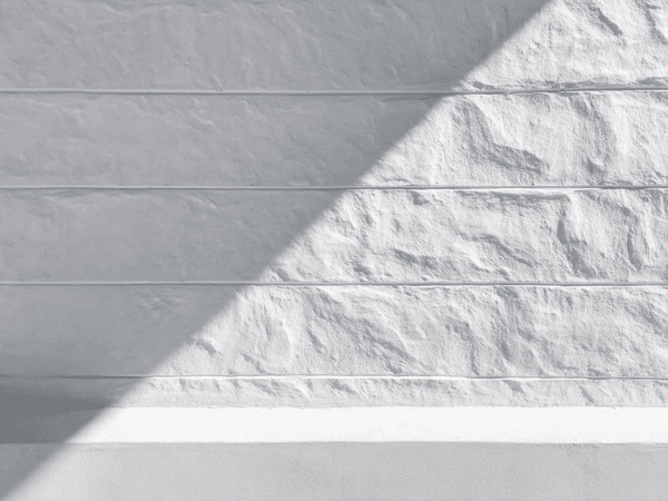 A white textured wall with horizontal lines is partially shaded by diagonal sunlight, creating a contrast between light and shadow.