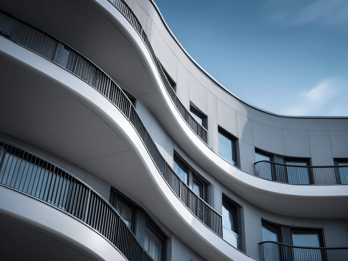 Curved modern building with smooth, wavy balconies and sleek railings against a clear blue sky.
