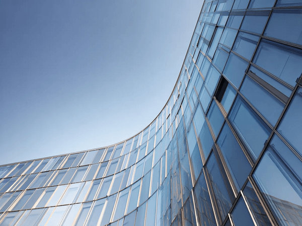 Curved glass building facade reflecting the blue sky, with a modern architectural design featuring vertical and horizontal lines.