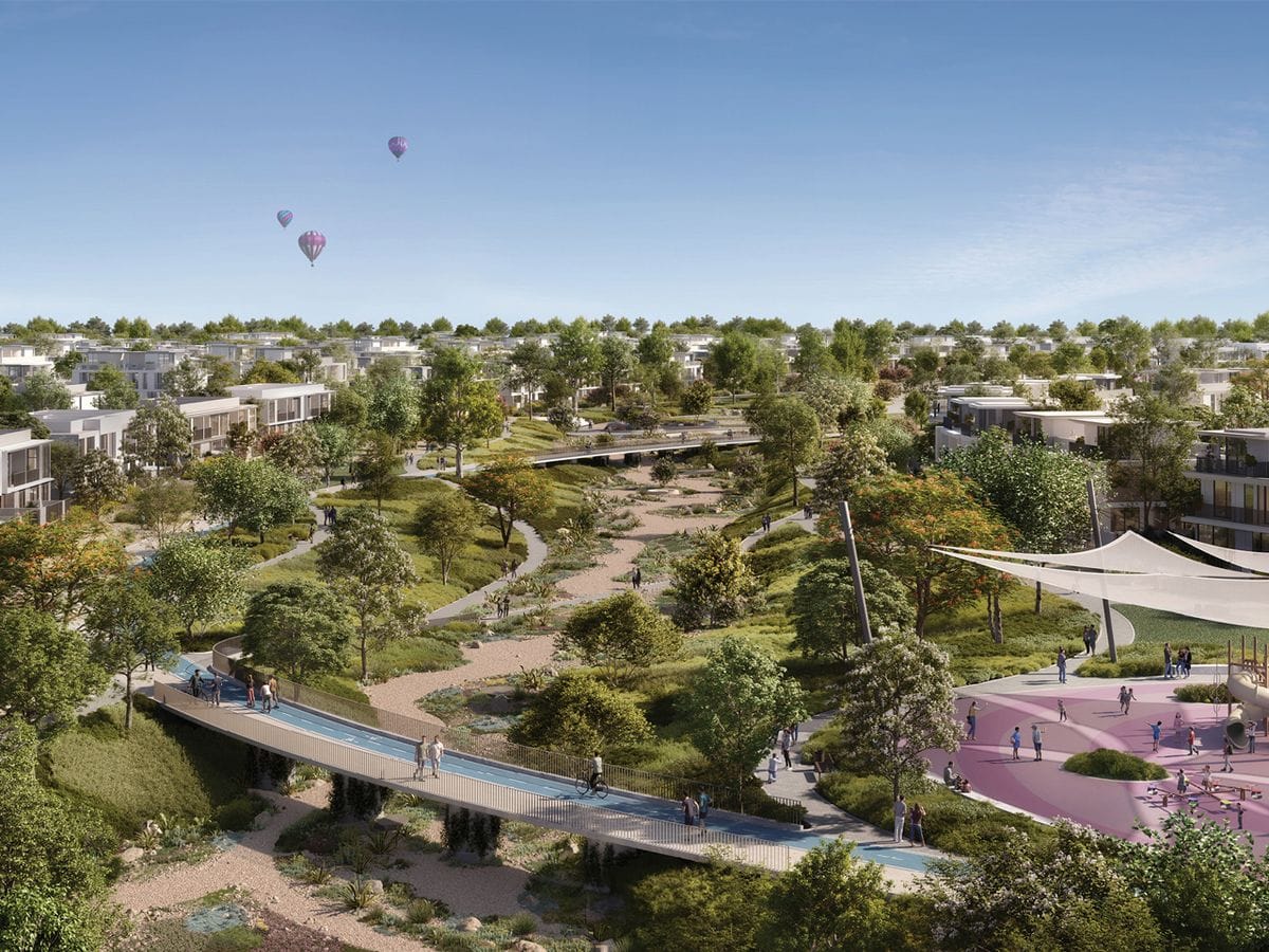 Luftaufnahme eines modernen Parks mit gewundenen Wegen, Grünflächen, einem Spielplatz und Heißluftballons am Himmel.