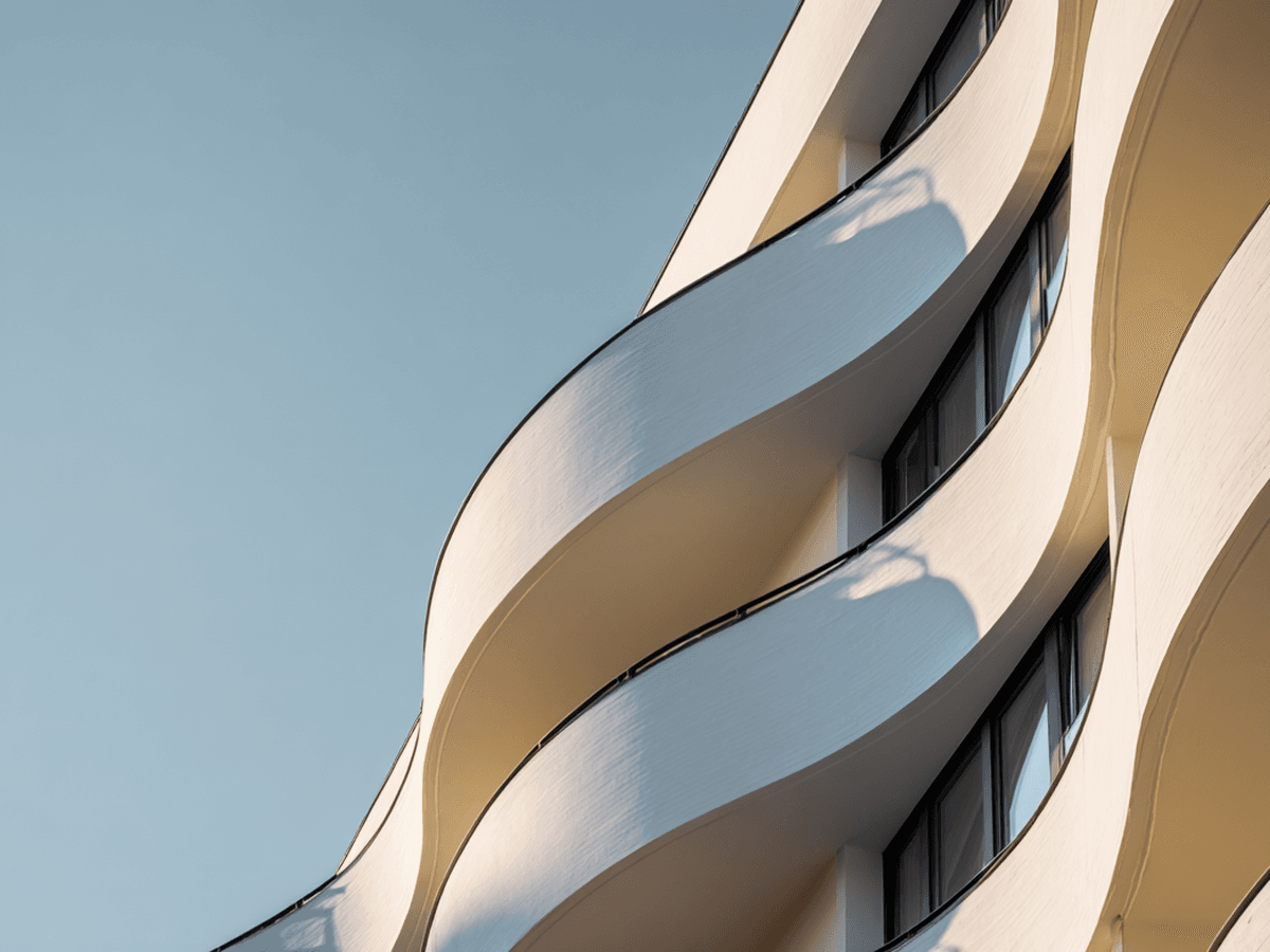 Curved, modern white building facade with large windows against a clear blue sky.