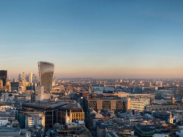 Panoramic view of London's skyline at sunset, featuring modern skyscrapers, the Shard, and the River Thames under a clear sky.