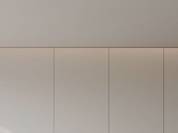 Minimalist interior featuring a curved ceiling with recessed lighting above a light beige wall with vertical panels.