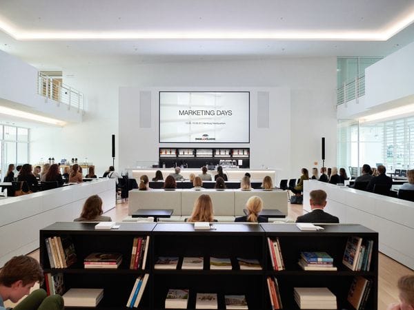 Publikum sitzt in einem hellen, modernen Saal für die "Marketing Days" von Engel & Völkers, Hauptsitz Hamburg. Bücherregale im Vordergrund.