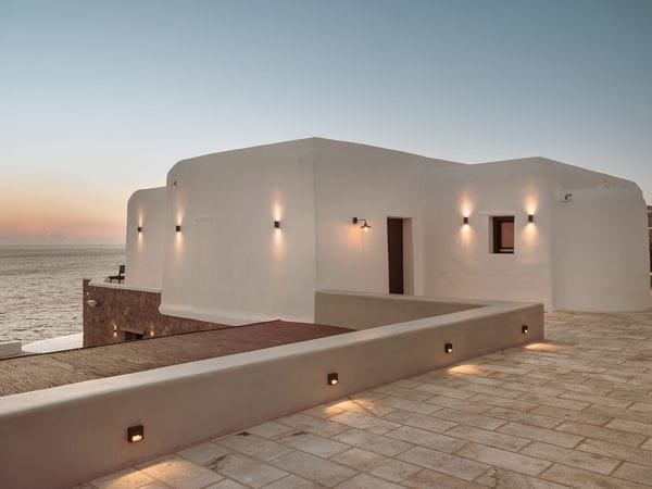 Außenansicht einer weißen Villa im mediterranen Stil mit einer Steinterrasse mit Blick auf das Meer bei Sonnenuntergang.