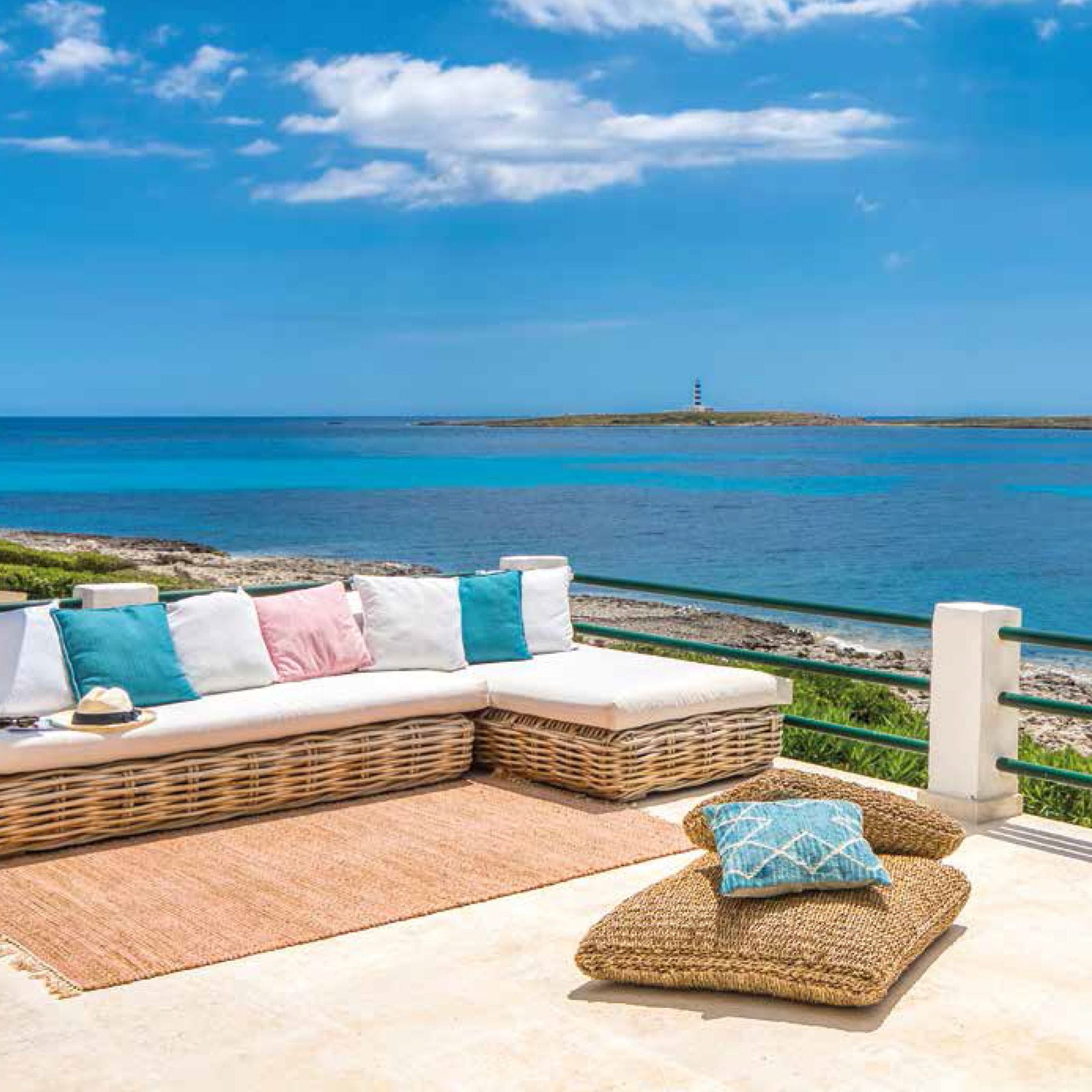 Outdoor patio with wicker sofa, pillows, and rug overlooking the ocean. A lighthouse is visible in the distance.