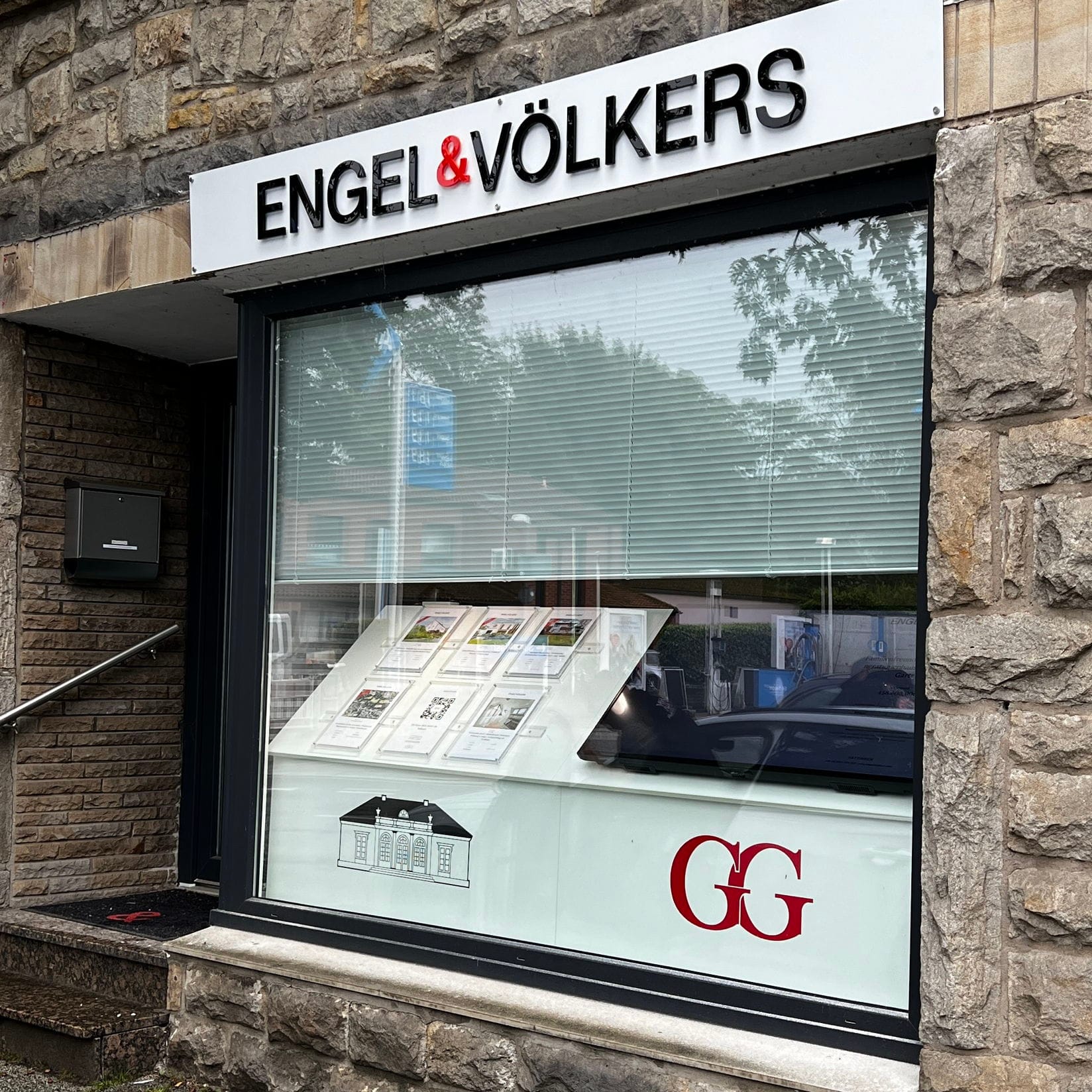 Exterior of Engel & Völkers real estate office with stone facade and window display of property listings.