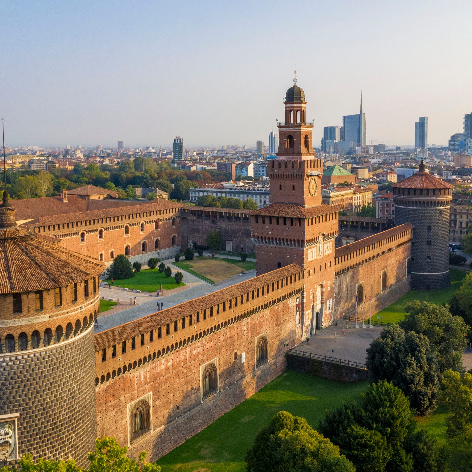 Luftaufnahme des Castello Sforzesco in Mailand, Italien. Rote Backsteinmauern und Türme, mit einem Uhrturm. Moderne Skyline der Stadt im Hintergrund.