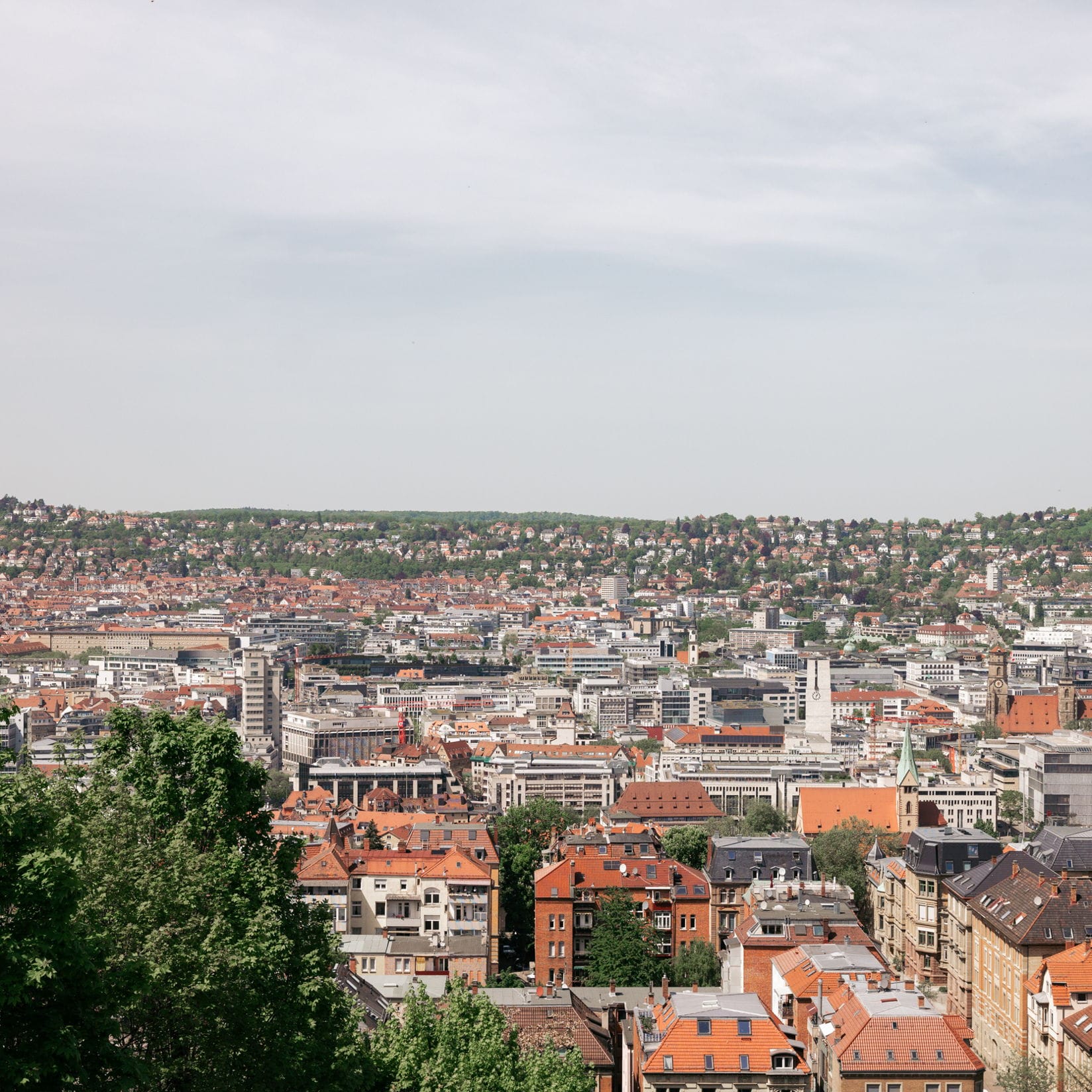 Stadtansicht von Stuttgart, Deutschland, mit rot gedeckten Gebäuden und grünen Bäumen unter einem bewölkten Himmel.