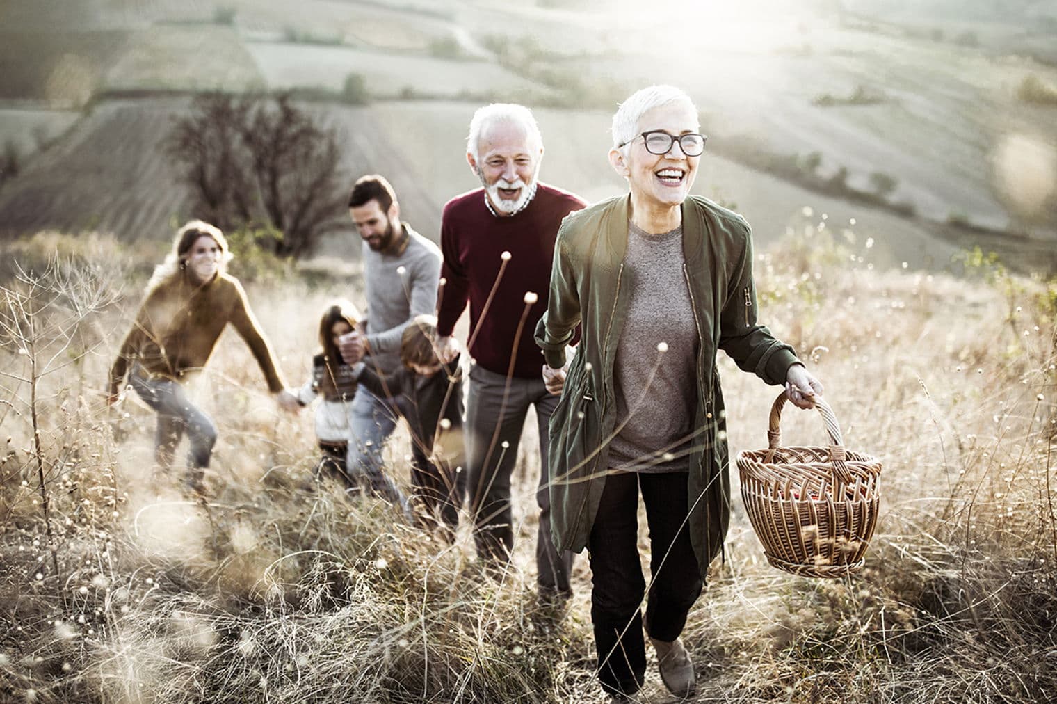 A multi-generational family walks through a field, smiling. The woman in front carries a woven basket.