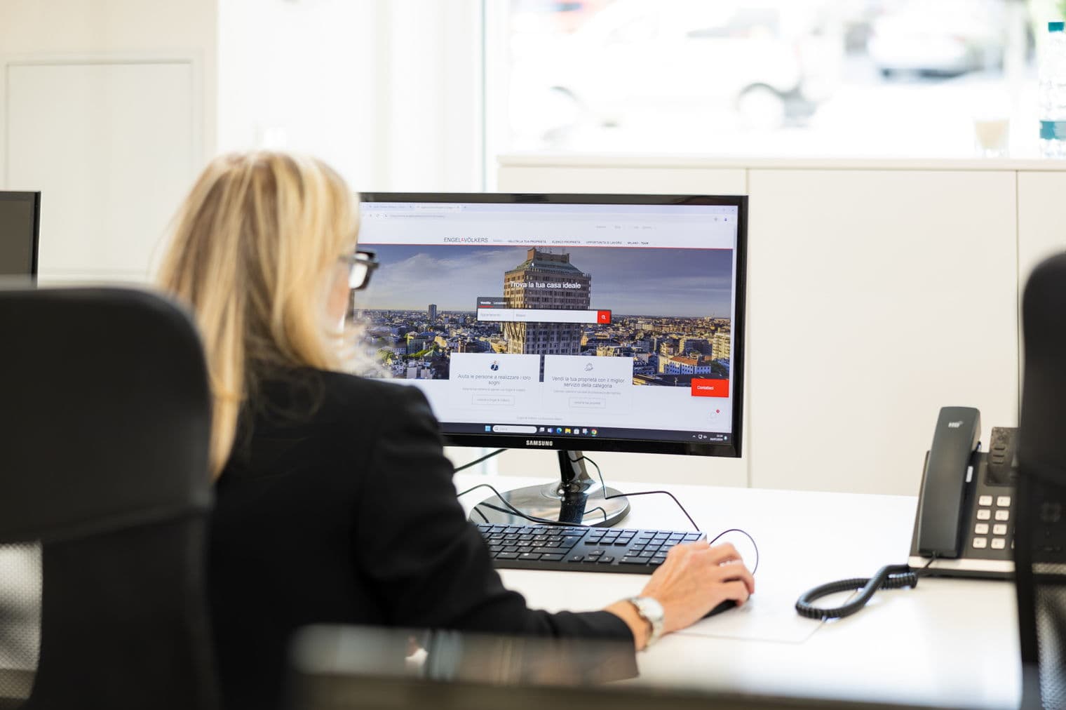 Eine Frau in einem schwarzen Anzug benutzt einen Computer, der die Engel & Völkers Website in einem hellen Büroumfeld anzeigt.