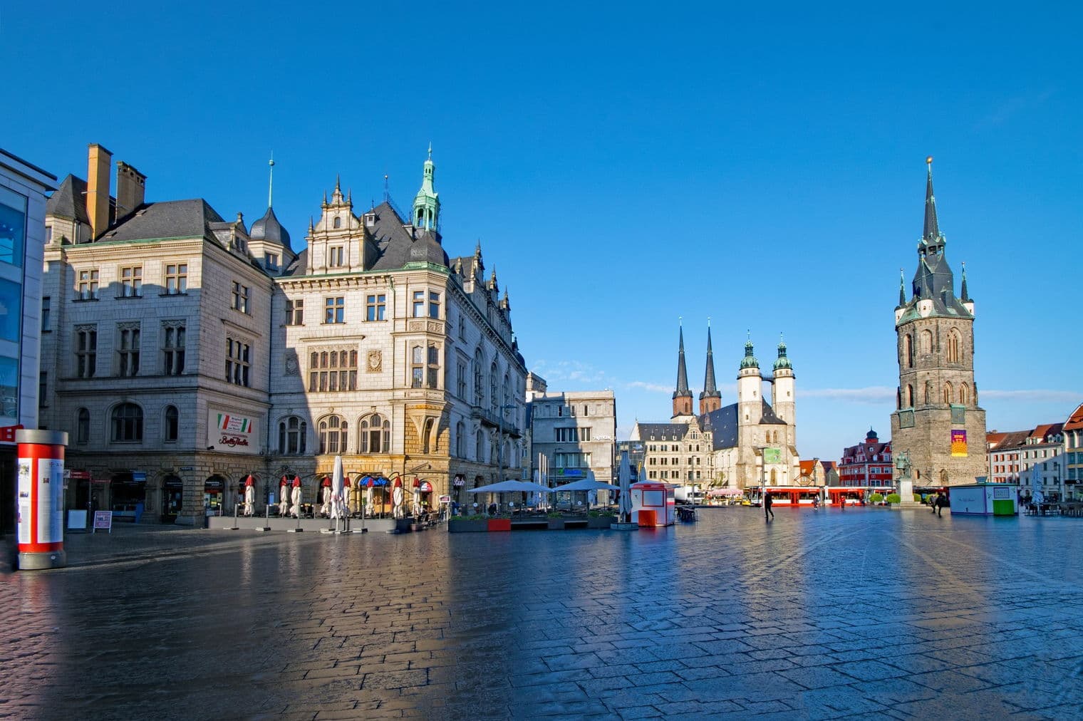 Stadtansicht von Halle (Saale), Deutschland, mit historischen Gebäuden, Kirchtürmen und einem großen, offenen Platz unter einem klaren, blauen Himmel.