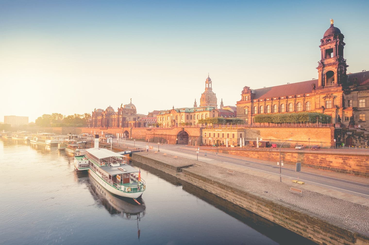 Dresden, Deutschland bei Sonnenaufgang. Boote auf der Elbe, mit historischen Gebäuden im Hintergrund. Warmes, goldenes Licht.